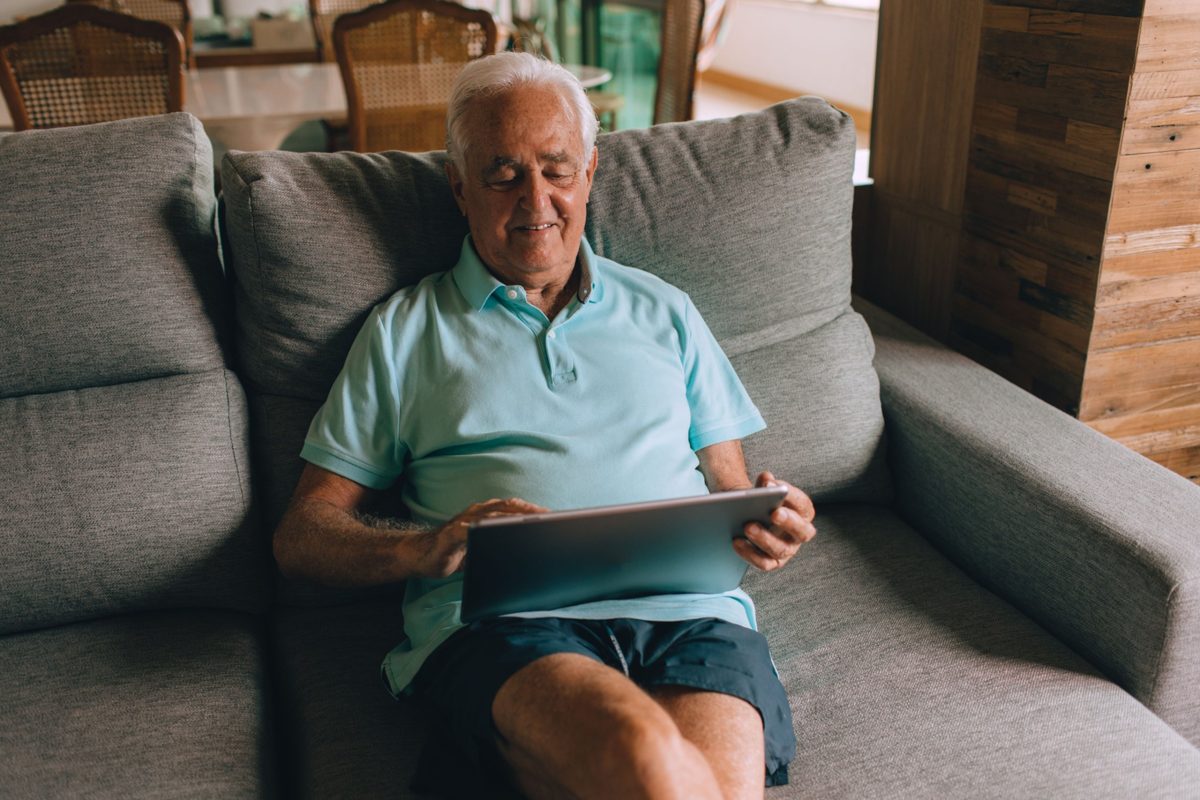 Senior man smiling while using a tablet at home